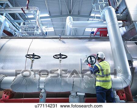 Stock Image - Worker turning valve of gas fired power station. Fotosearch
