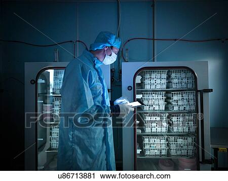 Stock Image - Worker using digital tablet to check archived electronic components in nitrogen atmosphere in clean room laboratory. Fotosearch