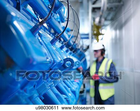 Stock Image - Worker with gas fired generator in gas fired power station. Fotosearch