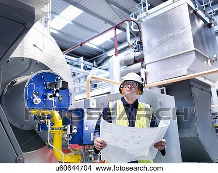 Picture - Worker with schematic drawings in gas fired power station. Fotosearch