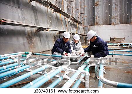 Stock Image - "Workers checking pipework on container ship at shipyard, GoSeong-gun, South Korea". Fotosearch