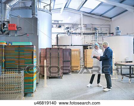 Stock Image - Workers in discussion by storage tanks in chocolate factory. Fotosearch