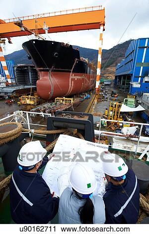 Stock Image - "Workers looking at plans at shipyard, GoSeong-gun, South Korea". Fotosearch