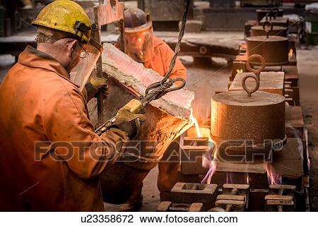 Stock Image - Workers pouring molten metal from flask in foundry. Fotosearch