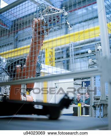Workers watching robot perform tasks in factory View Large Photo Image Stock Photo - Workers watching robot perform tasks in factory. Fotosearch