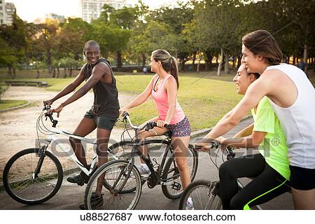 Young adults preparing to cycle in park View Large Photo Image Stock Photo - Young adults preparing to cycle in park. Fotosearch