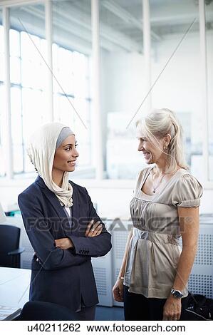 Young and mature businesswomen chatting in office View Large Photo Image Stock Image - Young and mature businesswomen chatting in office. Fotosearch