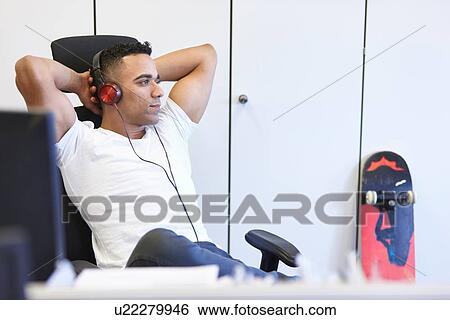 Young businessman relaxing and listening to headphones in office View Large Photo Image Stock Photograph - Young businessman relaxing and listening to headphones in office. Fotosearch