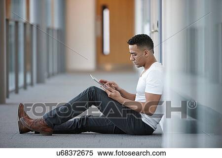 Young businessman sitting in office corridor using digital tablet View Large Photo Image Stock Photography - Young businessman sitting in office corridor using digital tablet. Fotosearch