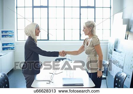 Young businesswoman and mature businesswoman shaking hands in office View Large Photo Image Stock Image - Young businesswoman and mature businesswoman shaking hands in office. Fotosearch