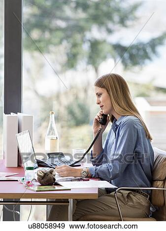 Stock Photo - Young businesswoman talking on telephone at home desk. Fotosearch