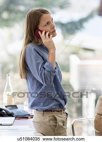 Young businesswoman talking on smartphone leaning against home desk View Large Photo Image Stock Photography - Young businesswoman talking on smartphone leaning against home desk. Fotosearch