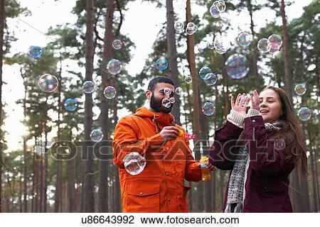 Stock Image - Young couple blowing bubbles in forest. Fotosearch