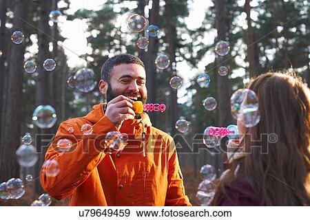 Stock Photo - Young couple blowing bubbles together in forest. Fotosearch