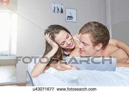 Young couple browsing digital tablet on bed View Large Photo Image Stock Photo - Young couple browsing digital tablet on bed. Fotosearch