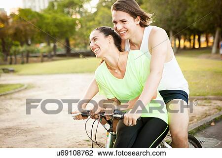 Stock Image - Young couple cycling pillion in park. Fotosearch