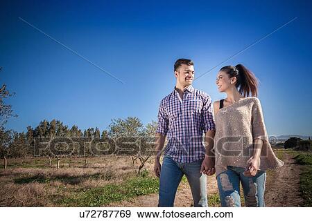 Young couple holding hands in field View Large Photo Image Stock Photo - Young couple holding hands in field. Fotosearch