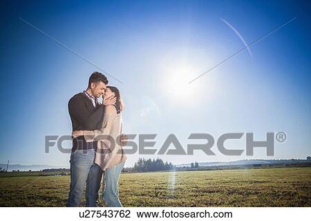 Stock Image - Young couple kissing in field. Fotosearch