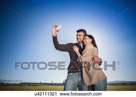Young couple photographing themselves against blue sky View Large Photo Image Stock Image - Young couple photographing themselves against blue sky. Fotosearch