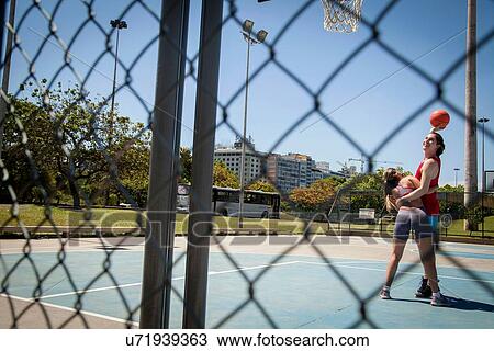 Stock Image - Young couple playing basketball on court. Fotosearch