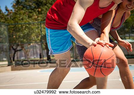 Stock Image - Young couple practicing basketball on court. Fotosearch