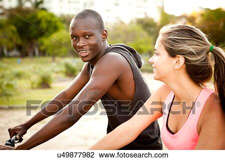 Stock Image - Young couple preparing to cycle in park. Fotosearch