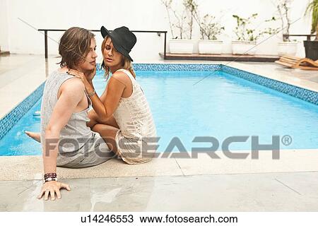 Stock Image - "Young couple sitting at rooftop swimming pool, Rio De Janeiro, Brazil". Fotosearch