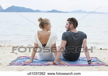Stock Image - "Young couple sitting on beach, Kradan, Thailand". Fotosearch