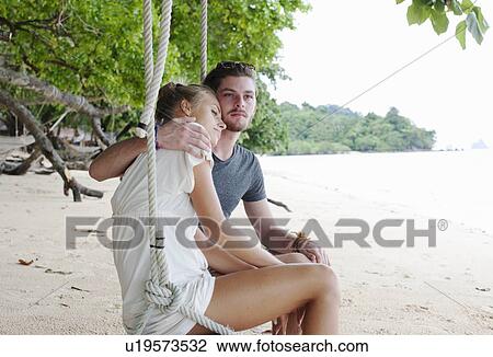 Stock Image - "Young couple sitting on beach swing, Kradan, Thailand". Fotosearch