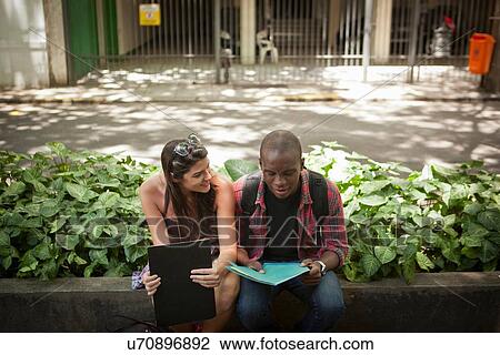 Stock Image - Young couple sitting on wall. Fotosearch