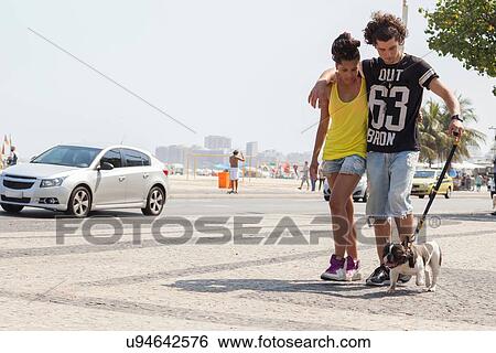Stock Photograph - "Young couple strolling with dog on sidewalk, Copacabana, Rio De Janeiro, Brazil". Fotosearch