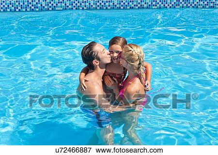 Stock Photo - "Young family in pool together, mother and father kissing daughter on cheek". Fotosearch