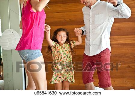Stock Image - Young family jumping on bed. Fotosearch