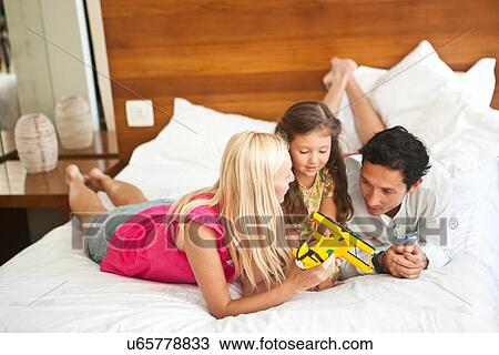 Stock Image - "Young family lying on bed, playing with toy plane". Fotosearch