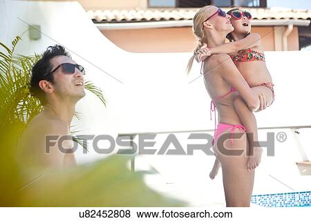 "Young family outdoors, wearing swimwear and sunglasses, mother holding daughter" View Large Photo Image Stock Photo - "Young family outdoors, wearing swimwear and sunglasses, mother holding daughter". Fotosearch