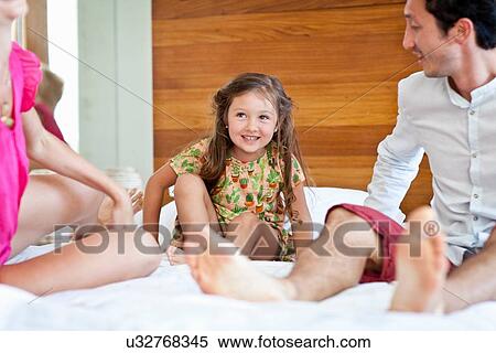 Stock Photography - Young family sitting on bed together. Fotosearch