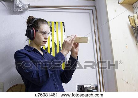 Stock Image - Young female carpenter checking timber in workshop. Fotosearch