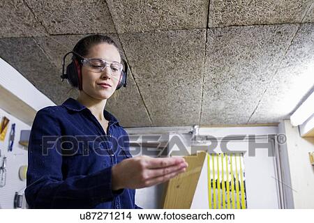 Picture - Young female carpenter examining timber in workshop. Fotosearch