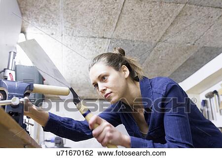 Stock Image - Young female carpenter shaping timber in workshop vice. Fotosearch