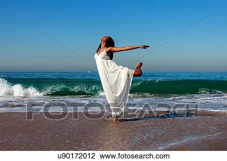 Stock Image - Young female dancer poised on one leg in ocean waves. Fotosearch