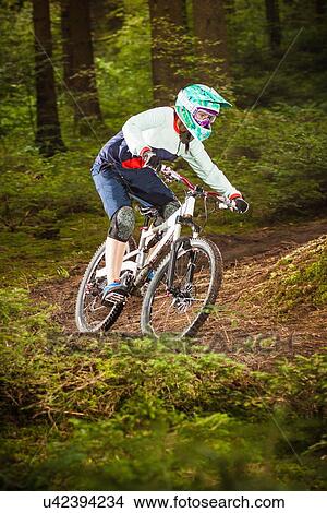Picture - Young female downhill mountain biking in forest. Fotosearch