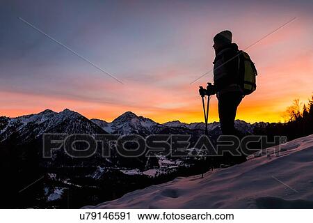 Stock Image - "Young female hiker looking out from mountainside at dusk, Reutte, Tyrol, Austria". Fotosearch