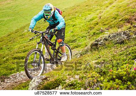 Stock Photo - Young female mountain biker cycling on hillside track. Fotosearch