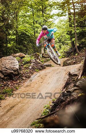 Stock Image - Young female mountain biker jumping mid air in forest. Fotosearch