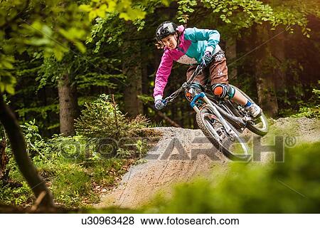 Stock Photo - Young female mountain biker jumping on forest track. Fotosearch