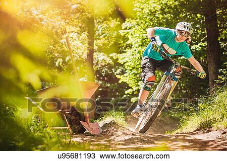 Stock Image - Young female mountain biker riding forest track. Fotosearch
