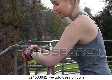 Stock Image - Young female runner checking stop watch in park. Fotosearch