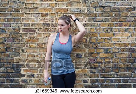 Young female runner leaning against brick wall taking a break View Large Photo Image Stock Photograph - Young female runner leaning against brick wall taking a break. Fotosearch