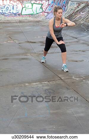 Young female runner warming up and checking stop watch in skatepark View Large Photo Image Picture - Young female runner warming up and checking stop watch in skatepark. Fotosearch