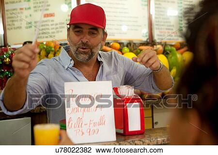 Stock Image - "Young female tourist buying juice at juice bar, Copacabana town, Rio De Janeiro, Brazil". Fotosearch